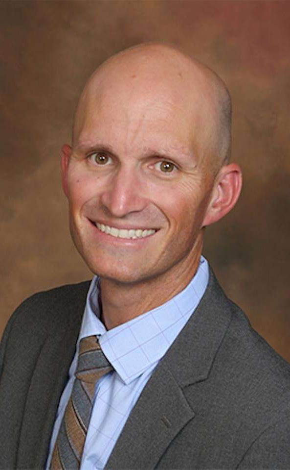 Tatum Pediatric Dentistry | Bald man named Dr. Farr in a professional suit and tie, smiling against a brown gradient background.